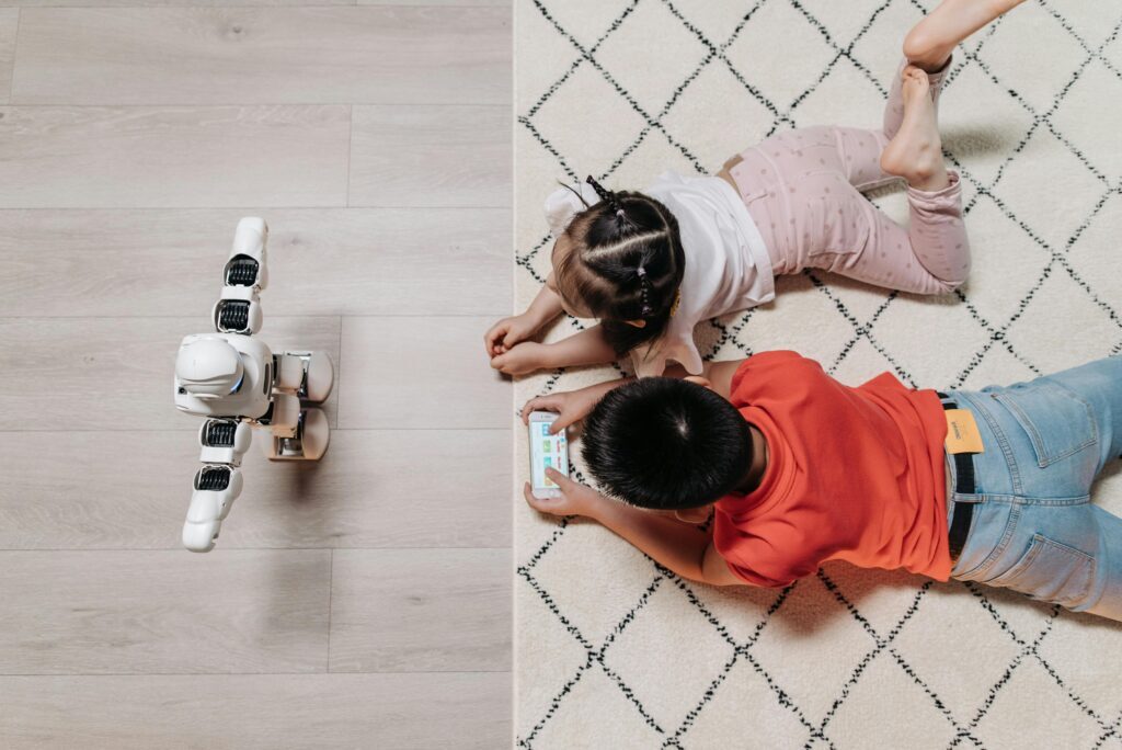 pexels-pavel-danilyuk-8295060 Two children lying on the floor interacting with a robot and a tablet, showcasing how the Best AI Tools make learning and play more engaging through technology.